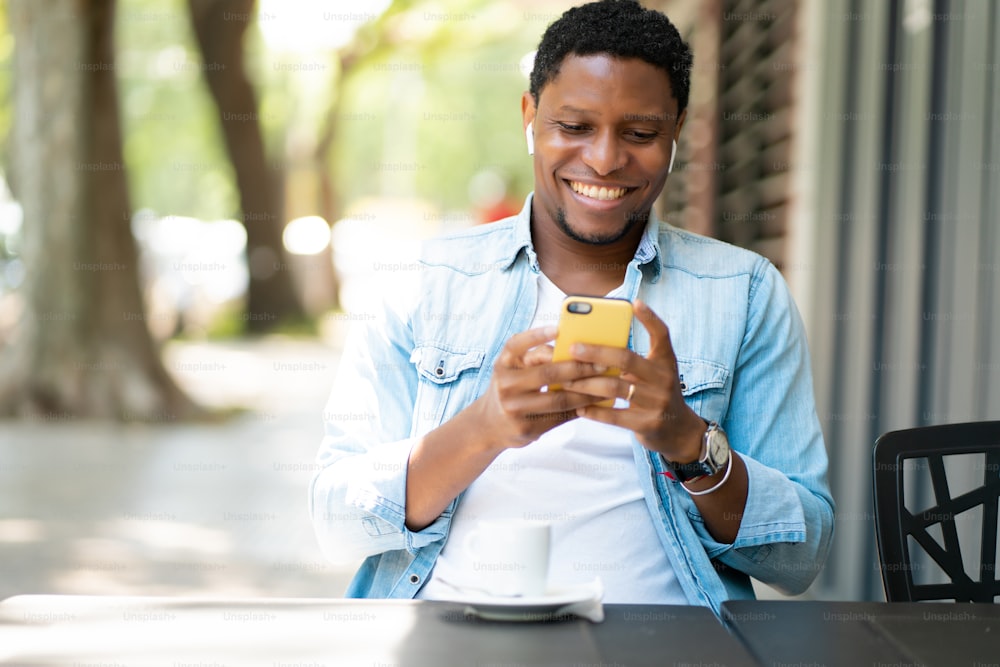 コーヒーショップに座りながら携帯電話でビデオ通話をしているアフリカ系アメリカ人の男性。アーバンコンセプト。