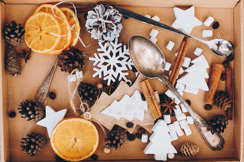 Christmas wooden decorations, anise star, cinnamon, dried oranges, pine cones, spoons, marshmallow in box on table. Top view. Winter holiday preparations.