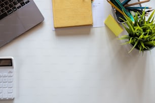 空白の画面のラップトップコンピュータ、ノートブック、マウス、コーヒーカップ、その他のオフィスを備えた白いオフィスデスクテーブル。コピースペースのある平面図
