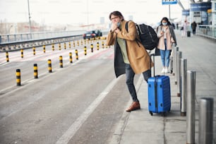Hübscher Herr mit Gepäckwagentasche, der pfeift, um das Taxi auf der Straße zu stoppen
