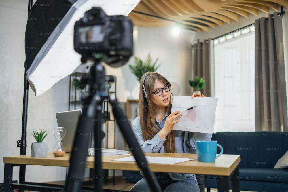 Attractive business woman in eyeglasses recording masterclass about success and finance. Pretty lady in headset using modern laptop, camera and soft box for work.