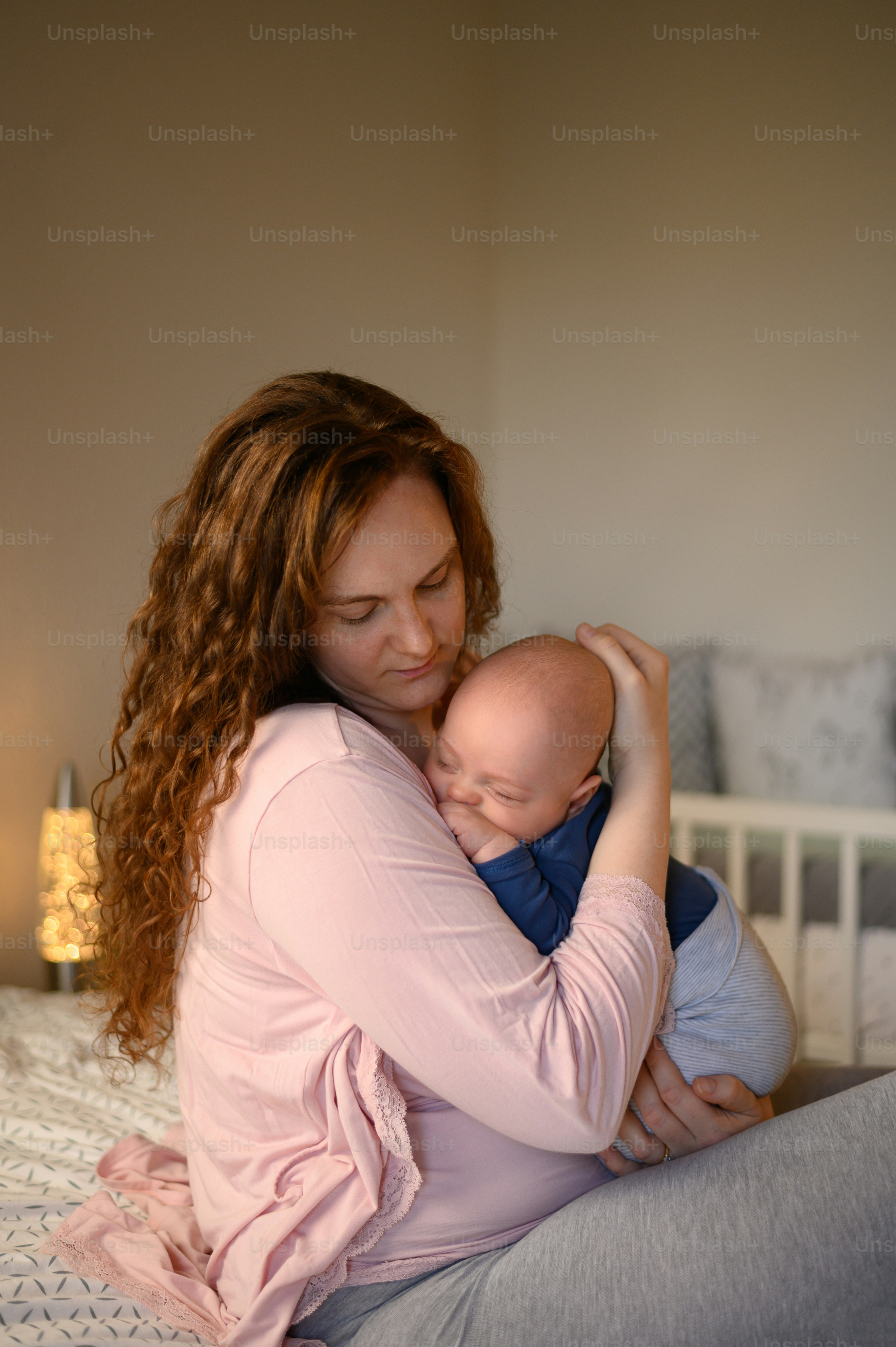 Mother holding her baby boy in her arms and singing him lullaby to fall asleep