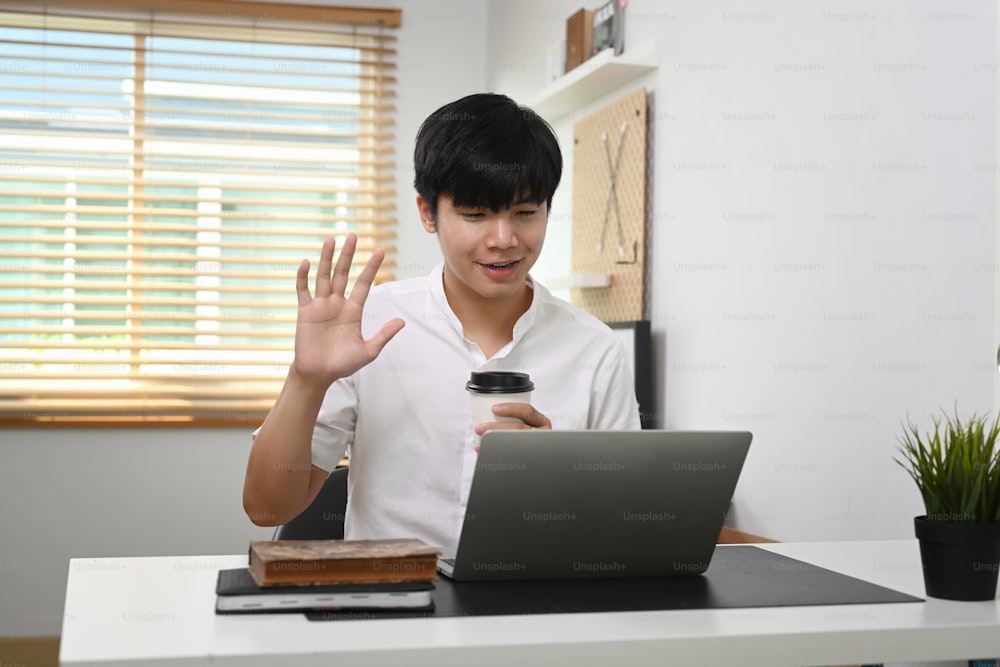 Smiling man holding coffee cup and having video call on laptop at home.