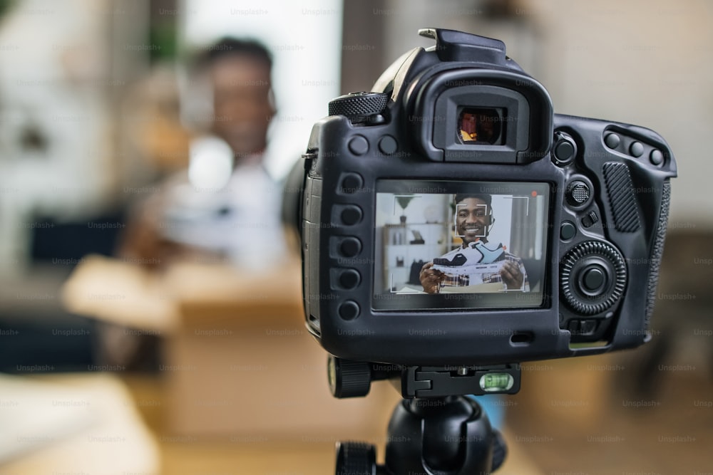 Afroamerikanischer Mann packt brandneue Turnschuhe zu Hause aus und nimmt Videos mit professioneller Kamera auf. Junger Blogger, der Online-Inhalte für seinen Kanal erstellt.