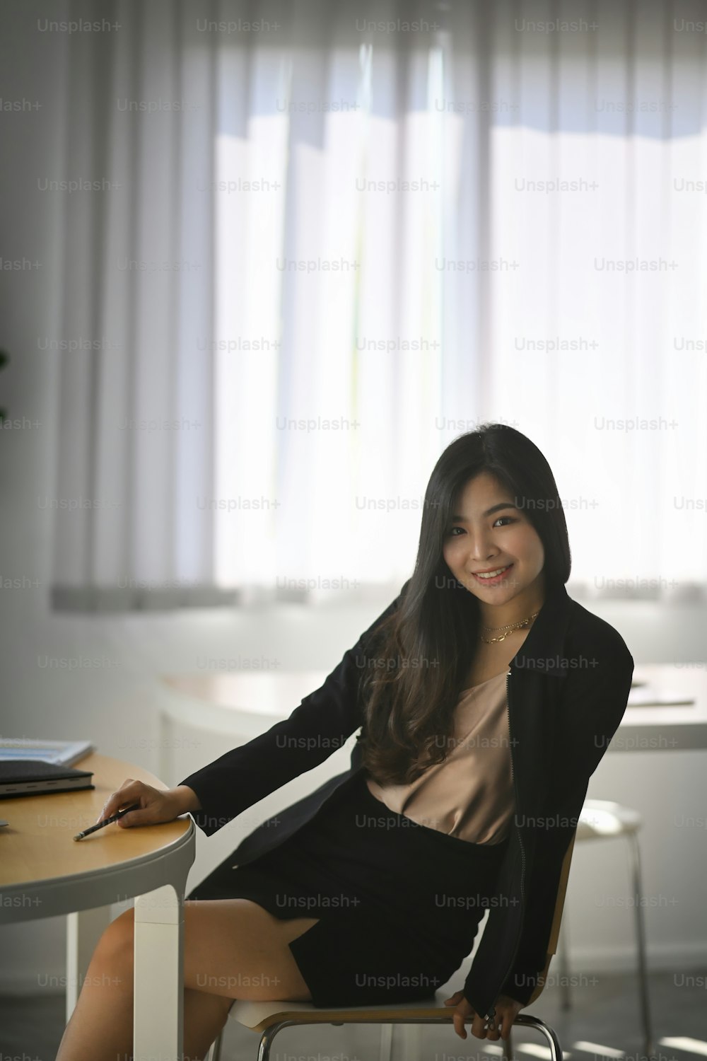 Portrait of cheerful young businesswoman sitting in modern office and smiling to camera.