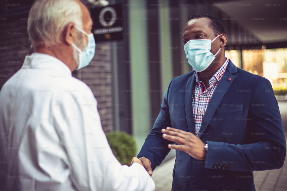 Business man, and doctor on street handshaking. Wearing protective mask. Focus background.