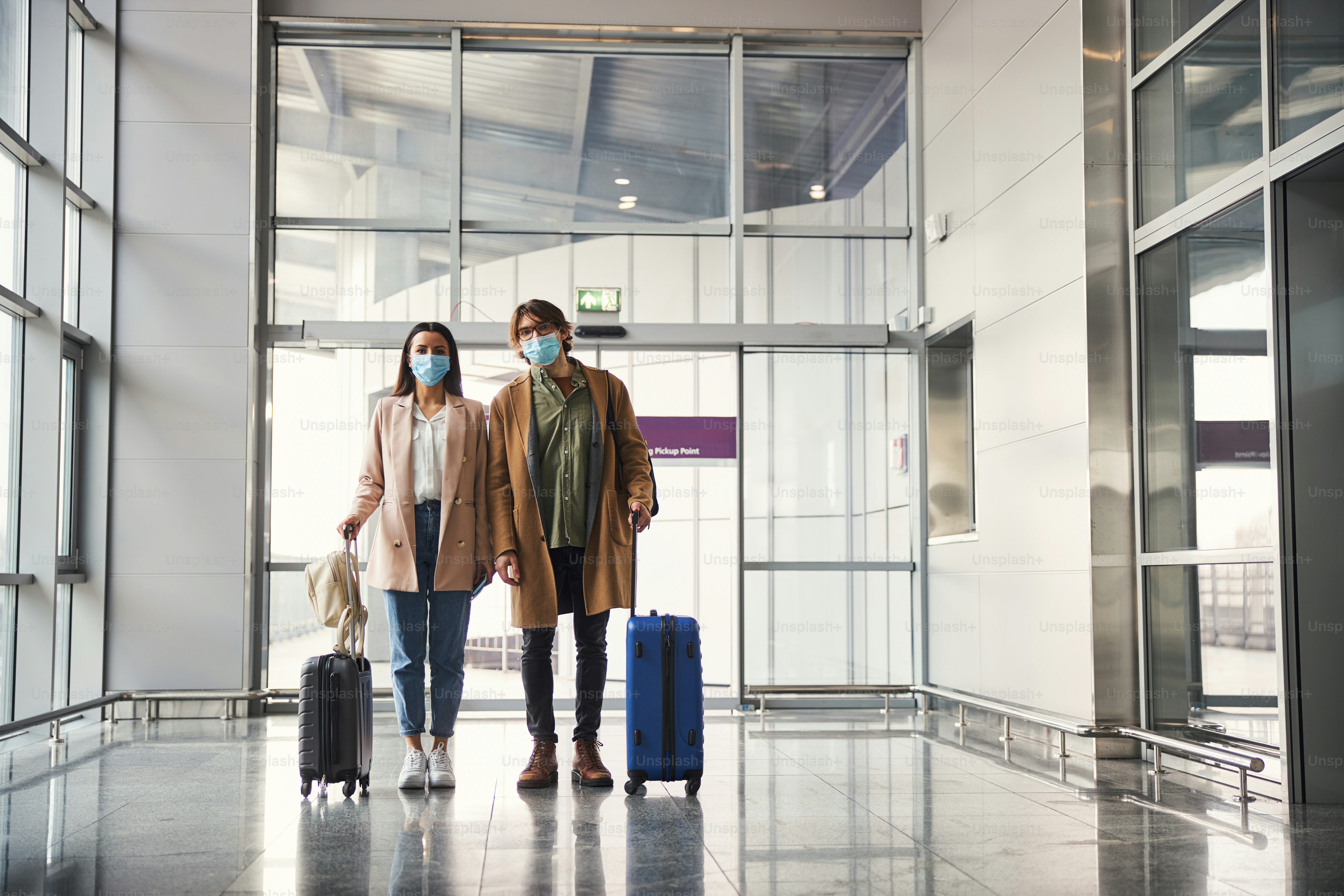 Elegant lady and gentleman with travel suitcases wearing protective face masks while waiting for the flight at airport