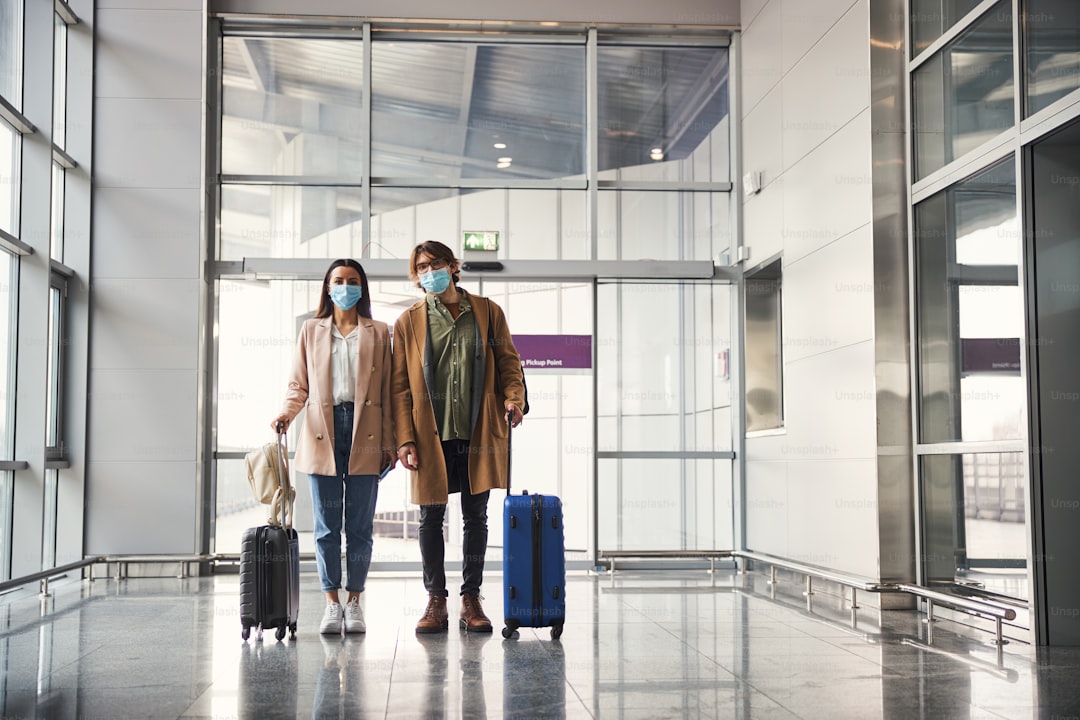 Elegant lady and gentleman with travel suitcases wearing protective face masks while waiting for the flight at airport