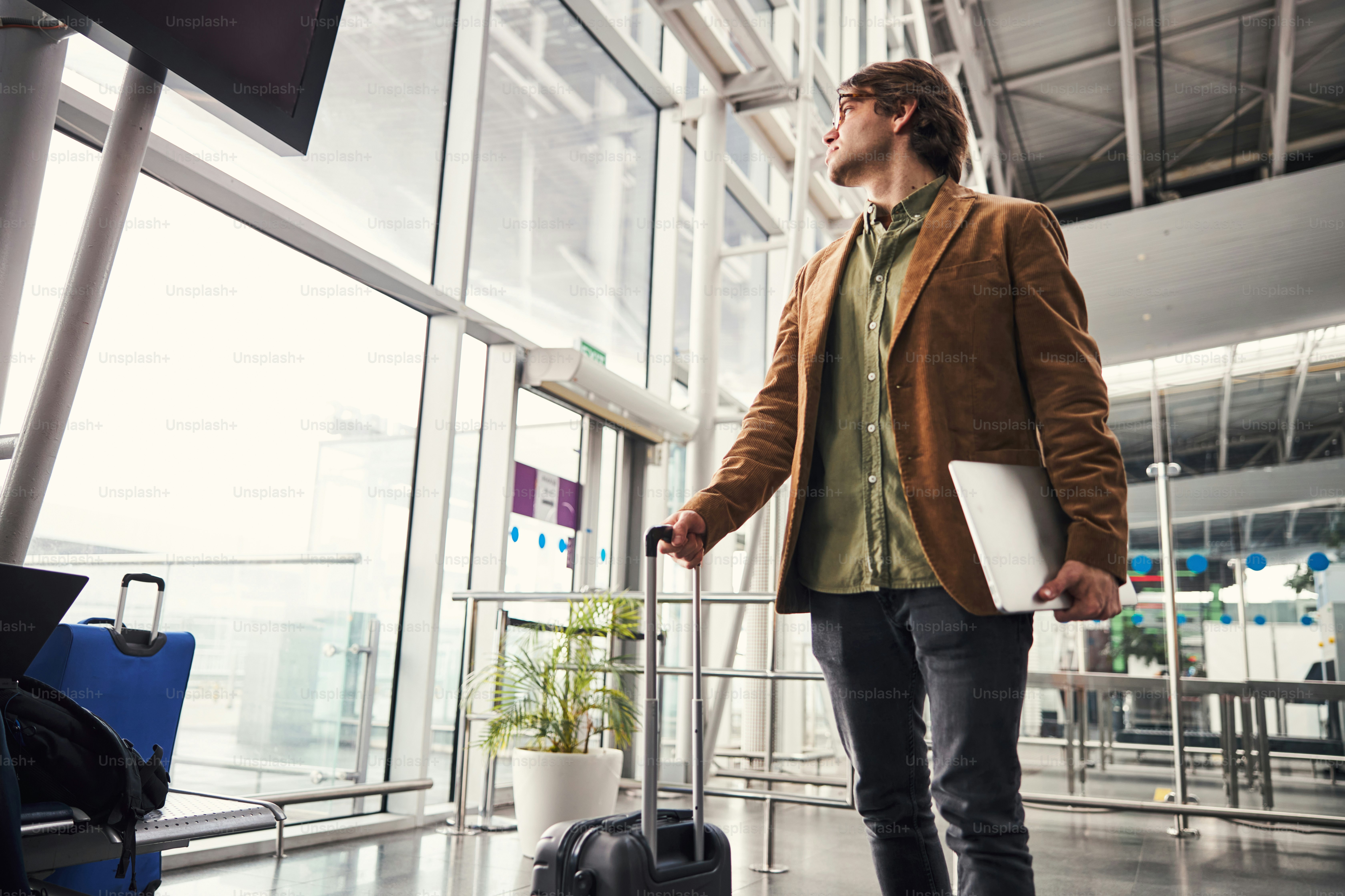 Handsome gentleman holding modern notebook and looking out the window while waiting for the flight at airport