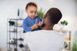 Back view of african father holding cute little son on hands that looking at camera. Happy active weekends at home. Family time.