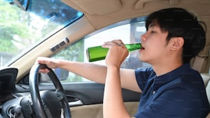 Joven asiático bebiendo cerveza mientras conduce un automóvil. Conducir bajo los efectos del alcohol.