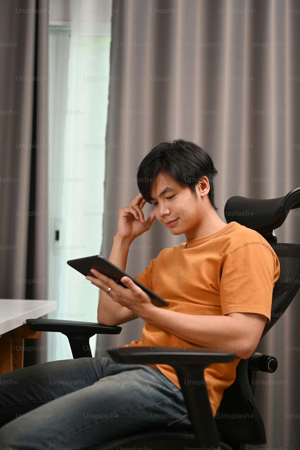 Portrait of young man freelancer sitting on comfortable chair and reading news on digital tablet.