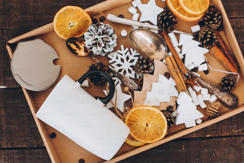 Christmas wooden decorations, cup, anise star, cinnamon, dried oranges, pine cones, spoons, marshmallow in box on table. Top view. Winter holiday preparations.