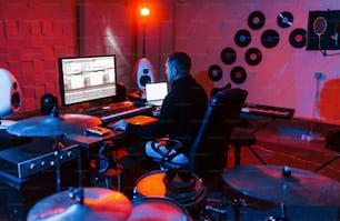 드럼 키트 근처의 스튜디오에서 실내에서 작업하고 음악을 믹싱하는 사운드 엔지니어.