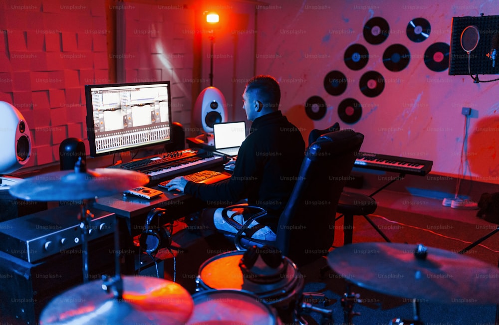 드럼 키트 근처의 스튜디오에서 실내에서 작업하고 음악을 믹싱하는 사운드 엔지니어.