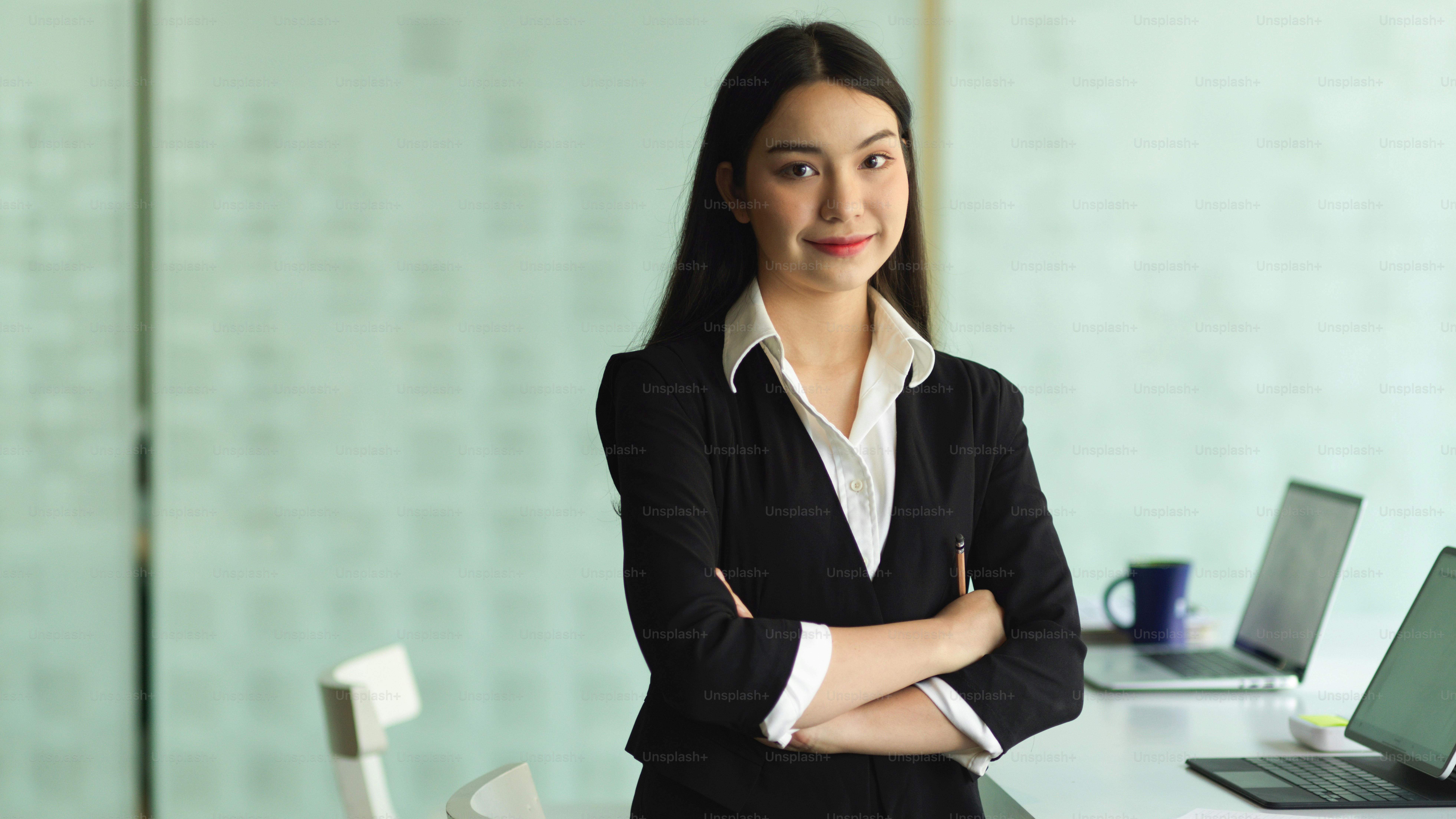Half-length portrait of young businesswoman in formal suit arms crossed and smiling to camera