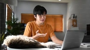 Smiling young asian man wearing earphones having video call with colleagues.