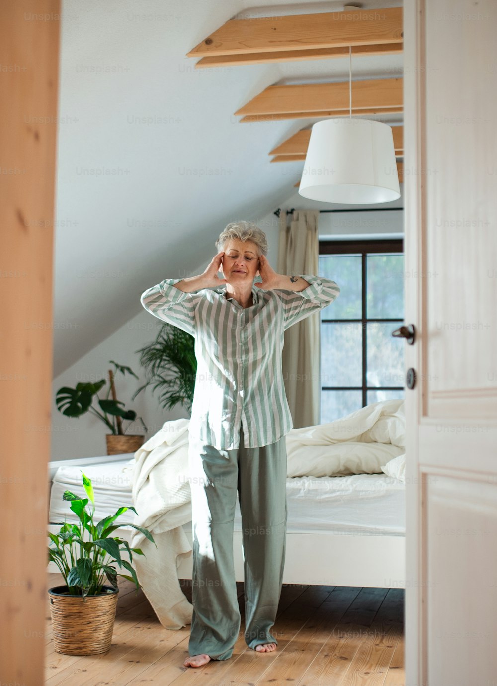 Happy senior woman in bed at home getting up in the morning, stretching.