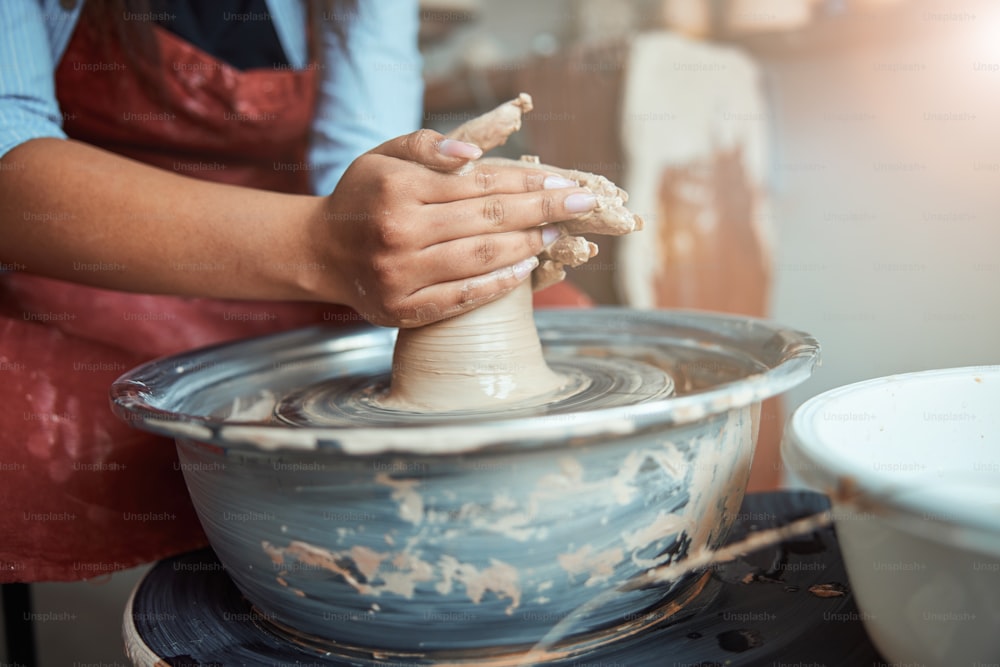 Primer plano de una joven ceramista que da forma a la arcilla en la rueda de alfarería mientras hace loza en el estudio de cerámica
