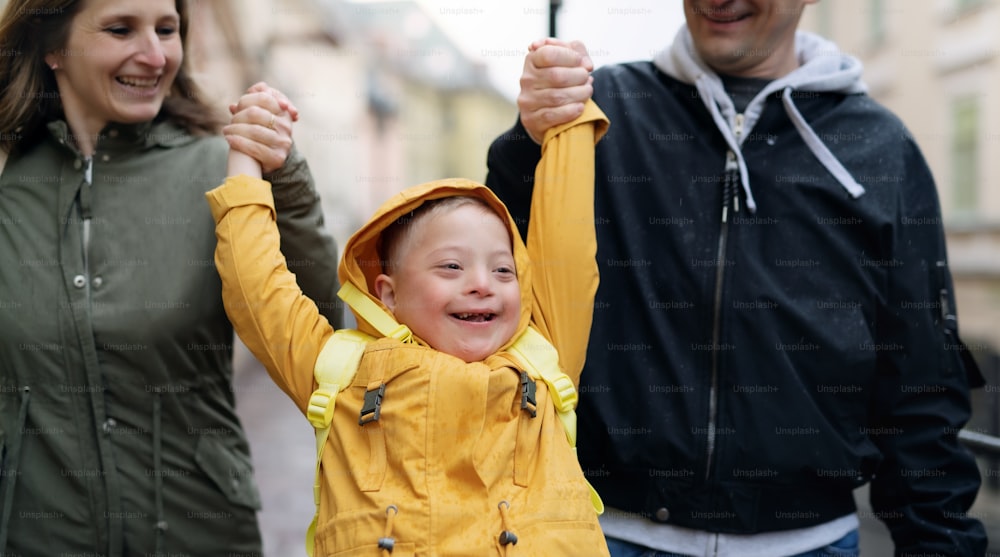 Portrait of happy family with down syndrome son outdoors on a walk in rain, having fun.
