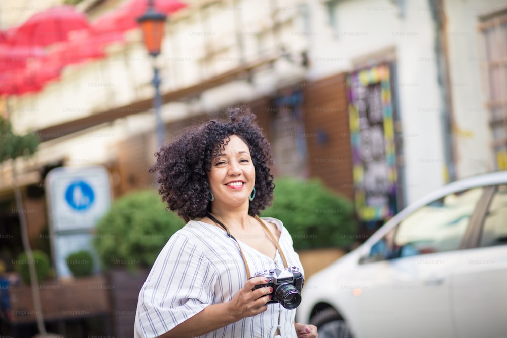Mujer alegremente turista corriendo por la calle.  Mujer sonriente con cámara en la calle.