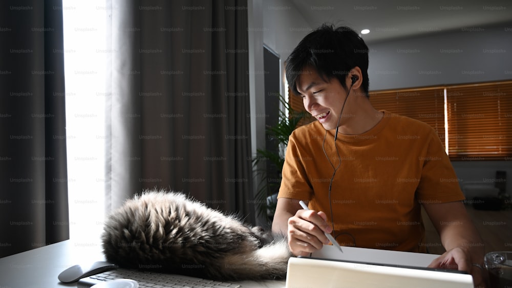 Happy man looking his cat and working online with digital tablet at home.