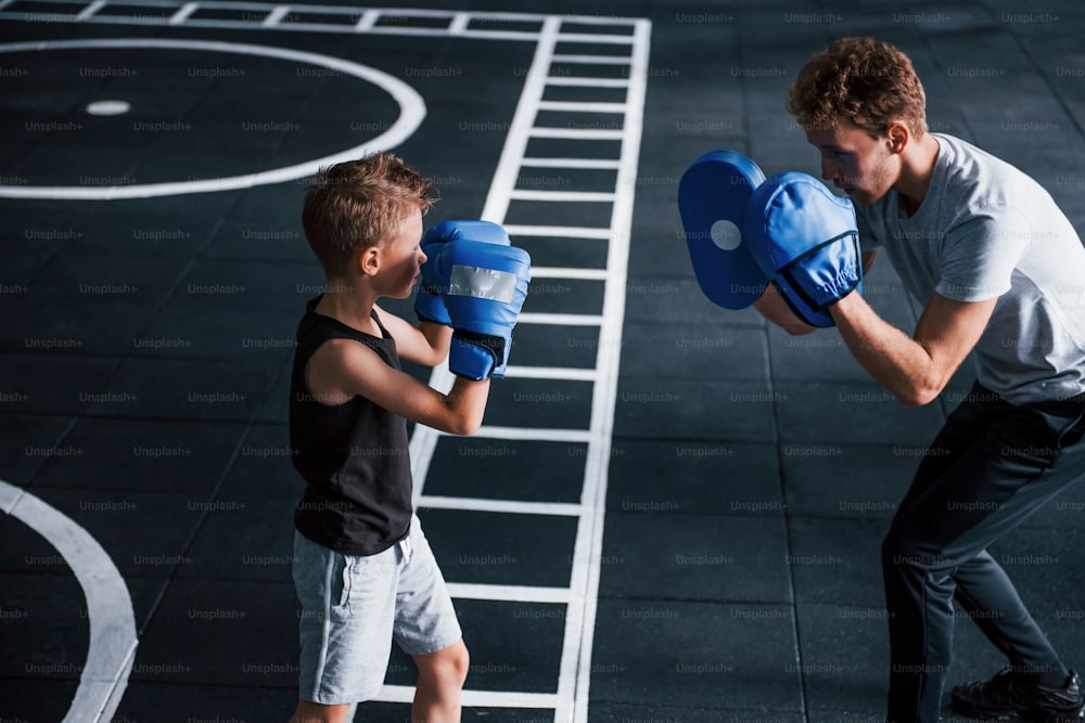 Young trainer teaches kid boxing sport in the gym.