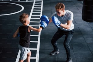 Young trainer teaches kid boxing sport in the gym.