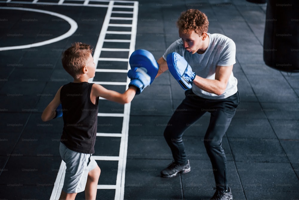 Young trainer teaches kid boxing sport in the gym.