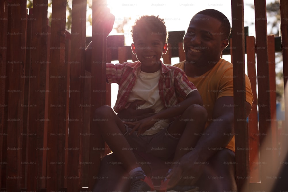 Father sitting with son on playground.  African American father and son outside.