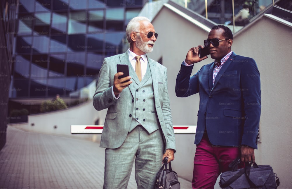 Two business men talking on the street. Using smart phones.