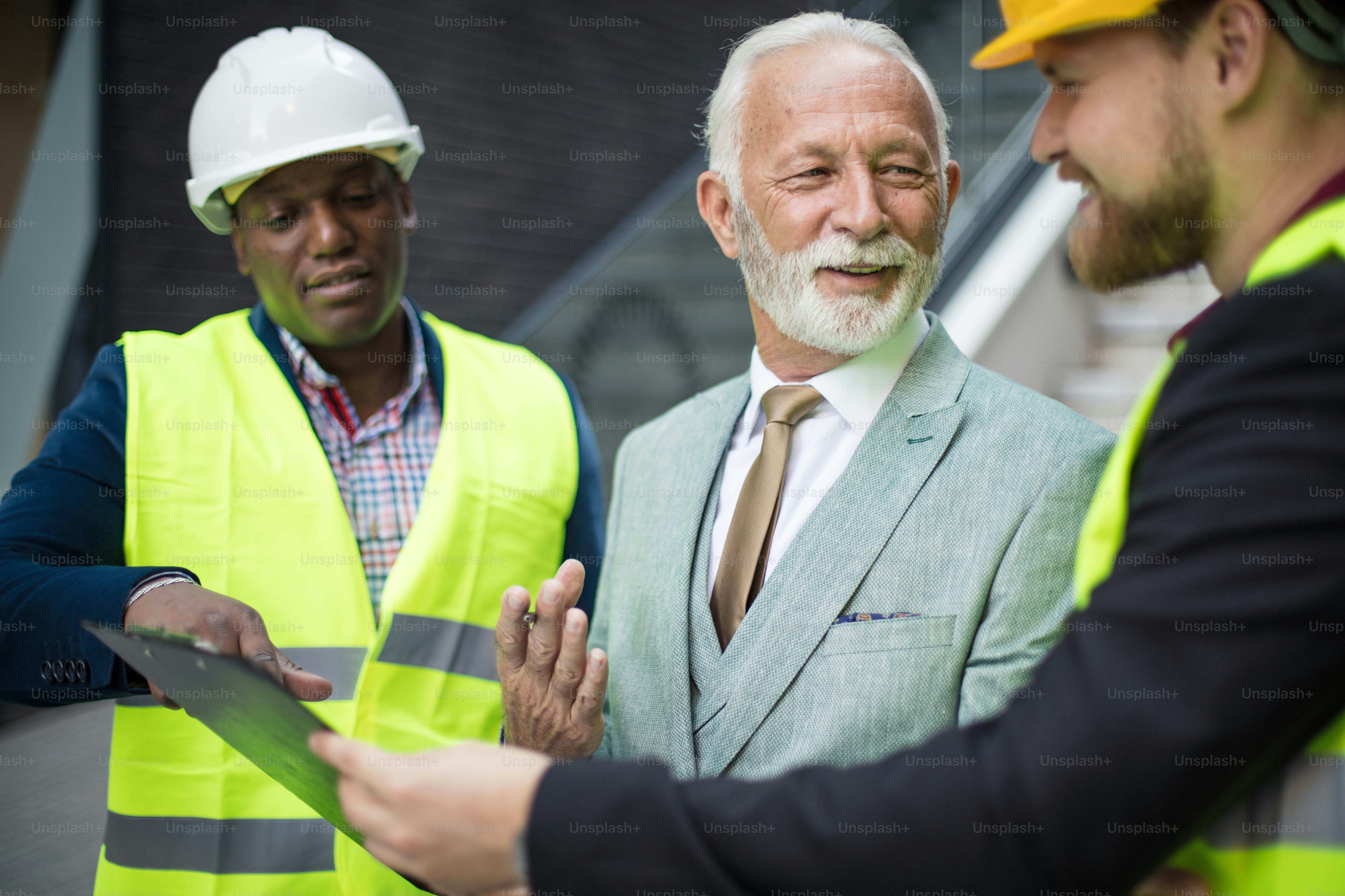 The construction site boss has a conversation with the architects. Focus is on background. Holding document
