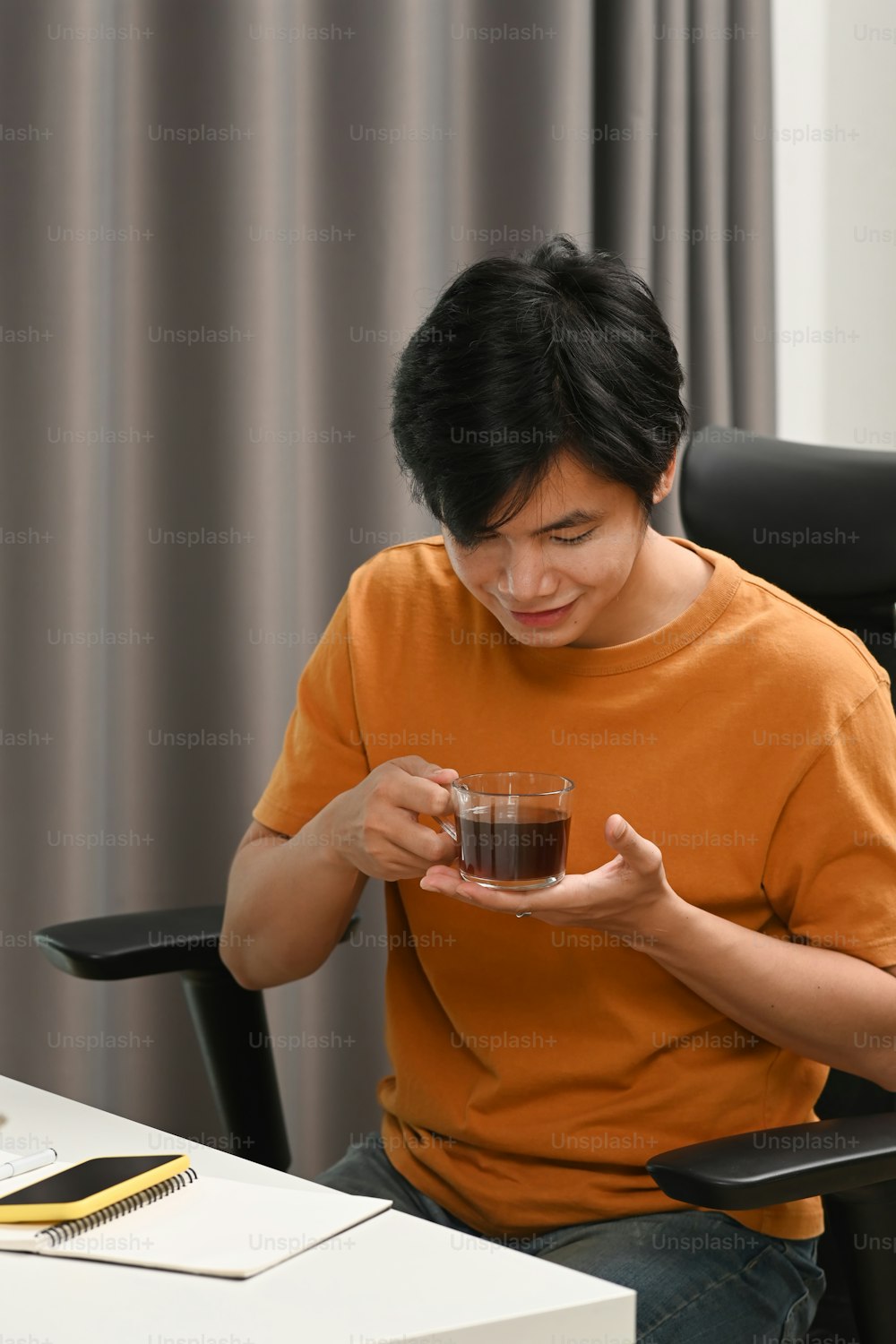 Portrait of young man drinking hot tea while sitting on office chair.