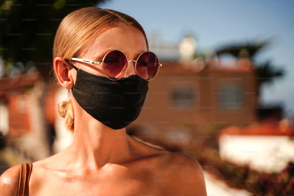Blonde young caucasian tourist wearing medical mask during relaxing walk. Fashionable look.