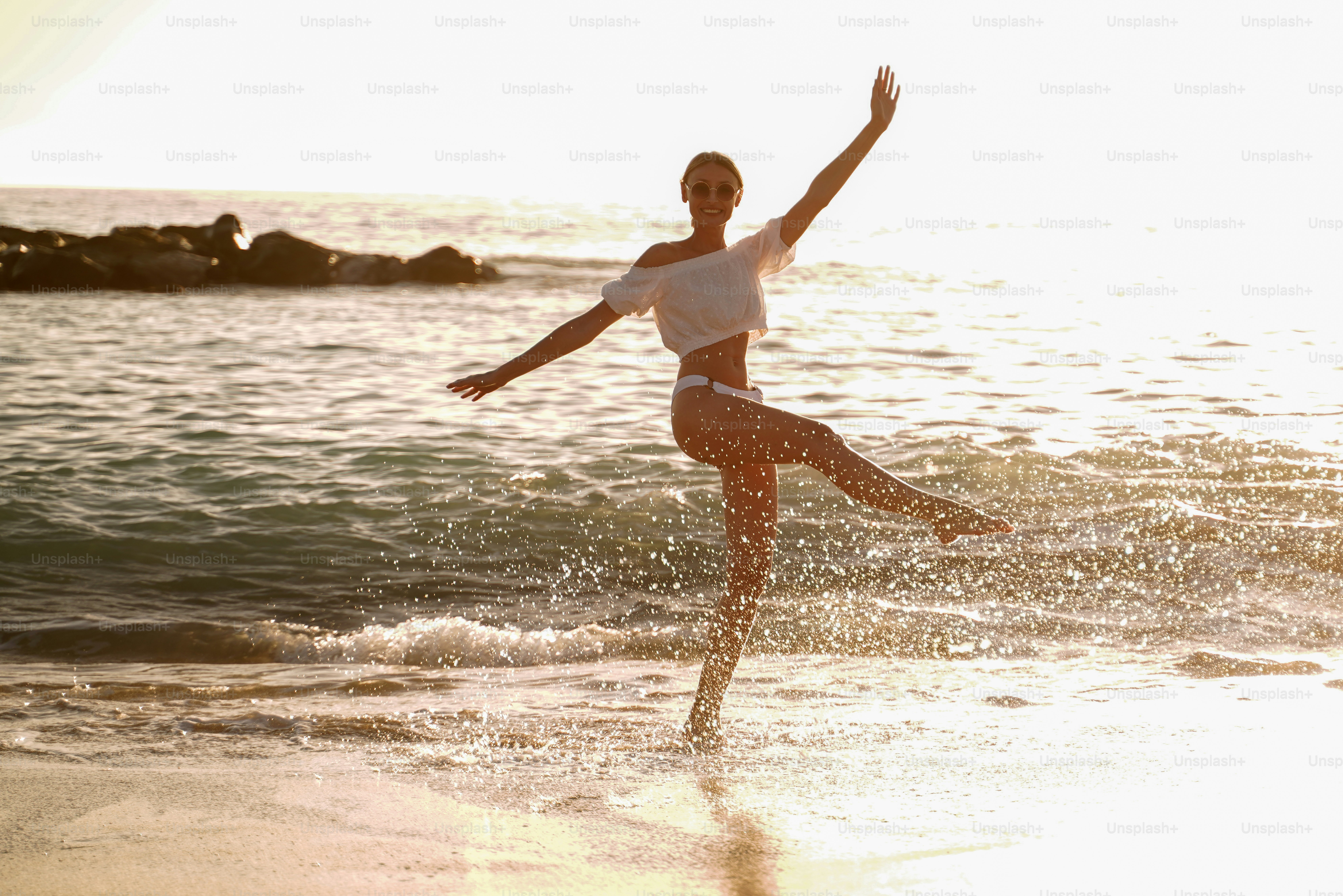 Beautiful caucasian woman playing in the water on the sandy beach at sunset sea shore. Summer vibes.
