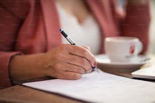 Geschäftsfrau sitzt im Café und schreibt auf Dokument. Der Fokus liegt auf der Hand.