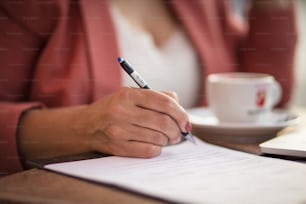 Femme d’affaires assise dans un café et écrivant sur un document. La concentration est à portée de main.