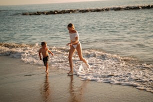Beautiful photo of happy family moment: woman with her little son playing and having fun on the beach during sunset. Summer vibes. Vacation concept.
