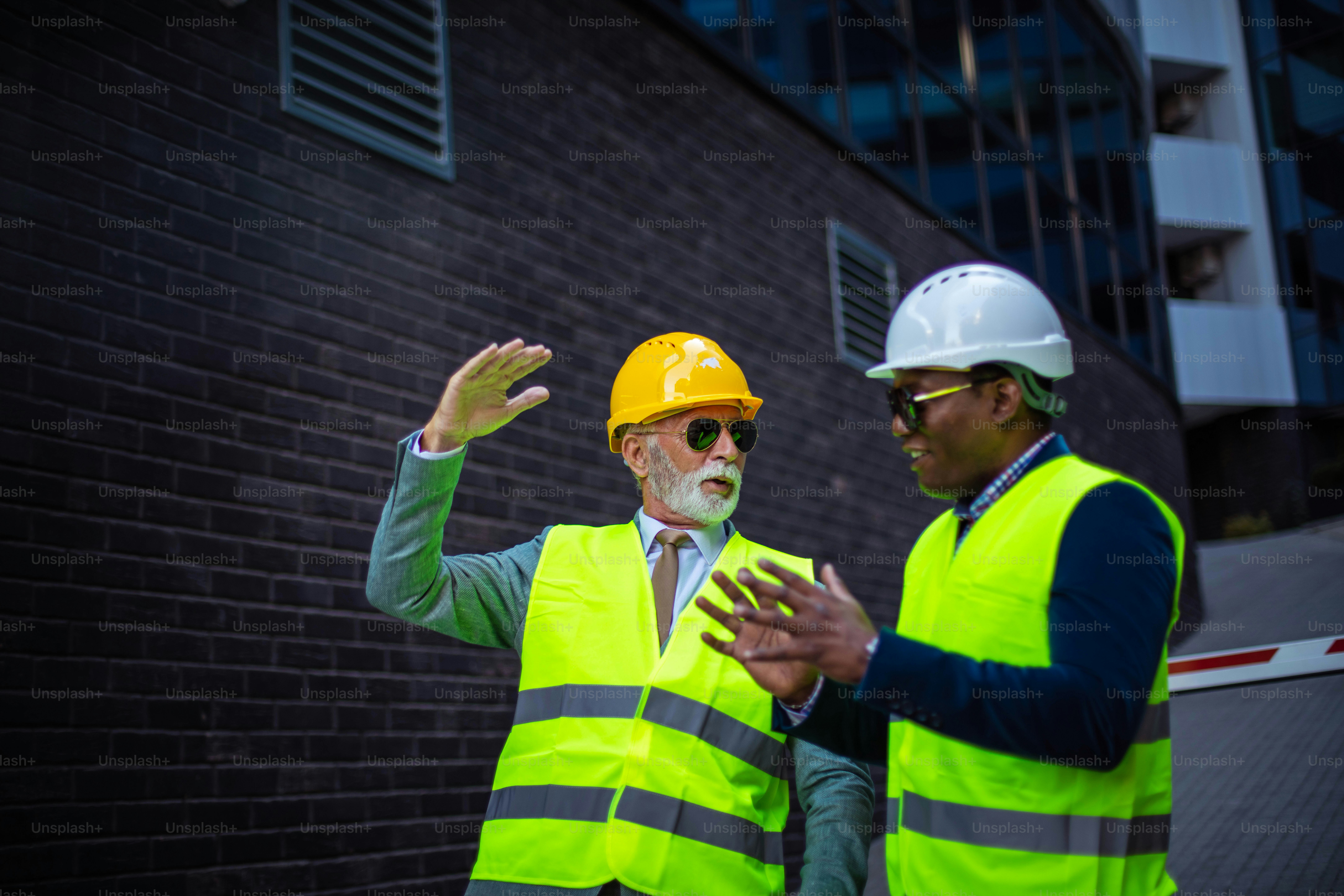 Mature engineer discussing the structure of the building with architects colleague at construction site. Businessmen talking