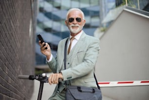Hombre de negocios senior con scooter eléctrico en la ciudad. Usando un teléfono inteligente.
