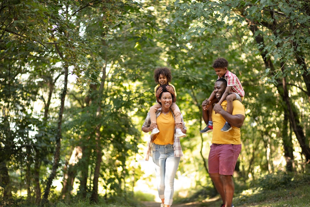 Famille afro-américaine marchant dans le parc. Des parents portant leurs enfants sur un support de ferroutage.
