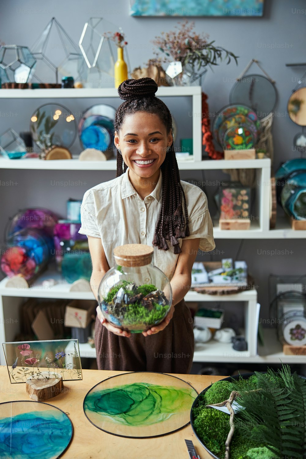 Front view of a smiling floral decorator holding a round glass jar plant terrarium with a cork lid