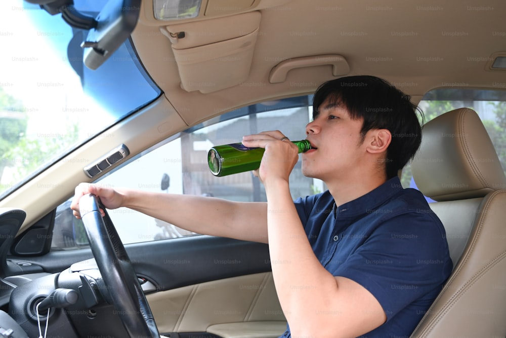 Fahren unter Alkoholeinfluss. Junger Mann, der Bier trinkt, während er ein Auto fährt.