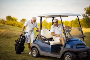Due golfisti uomini anziani in campo. Uomo seduto in carrello da golf.