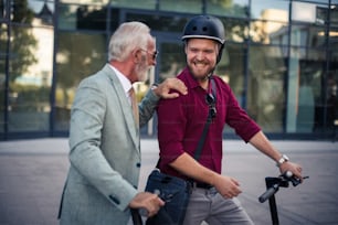 Hablando de trabajo.  Dos hombres de negocios montando un scooter eléctrico en la ciudad.