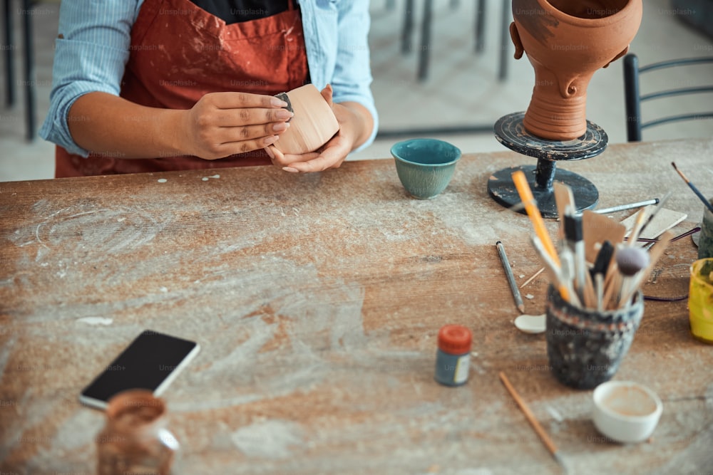 Primer plano de una joven artista de cerámica usando papel de lija mientras pule y alisa la loza en el estudio de cerámica