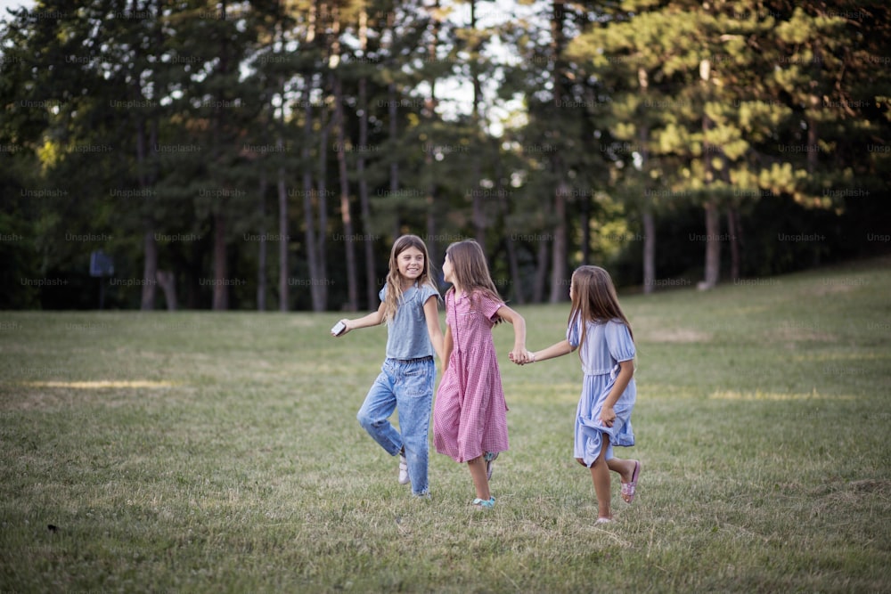 Three smiling little girls running trough nature and holding hands.