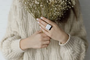 Beautiful stylish woman with modern square ring holding dried flowers. Fashionable female in sweater with unusual fused glass accessories and white manicure. Beauty and care concept
