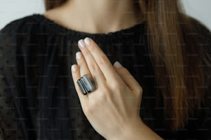 Beautiful stylish woman with modern square black ring on hand and white manicure, closeup. Fashionable female in black dress with unusual fused glass accessory. Beauty and care.