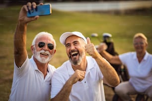 Golfeurs seniors utilisant leur téléphone et prenant un autoportrait. La mise au point se fait sur le premier plan.